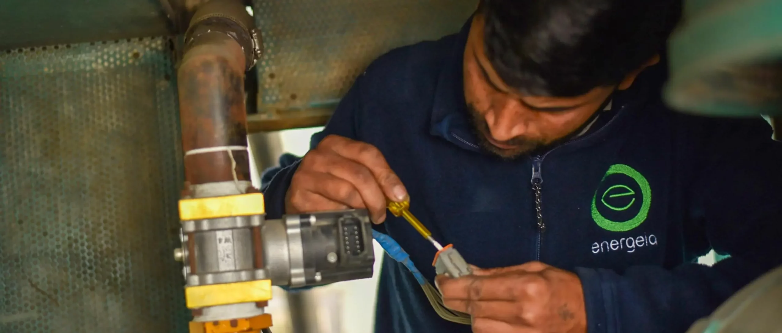 Technician in a blue uniform operating an industrial control panel inside a factory.