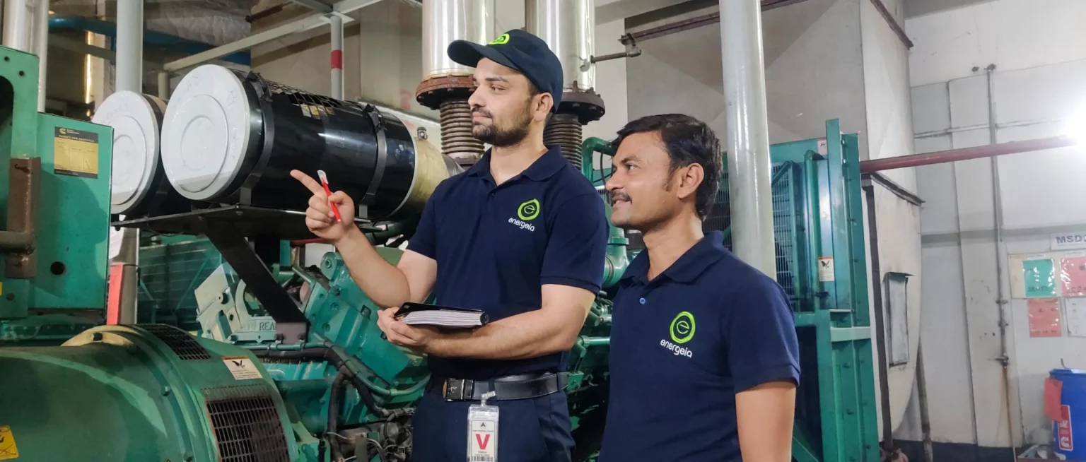 Two technicians in blue Energeia uniforms discussing an industrial system inside a factory, with one pointing towards equipment.