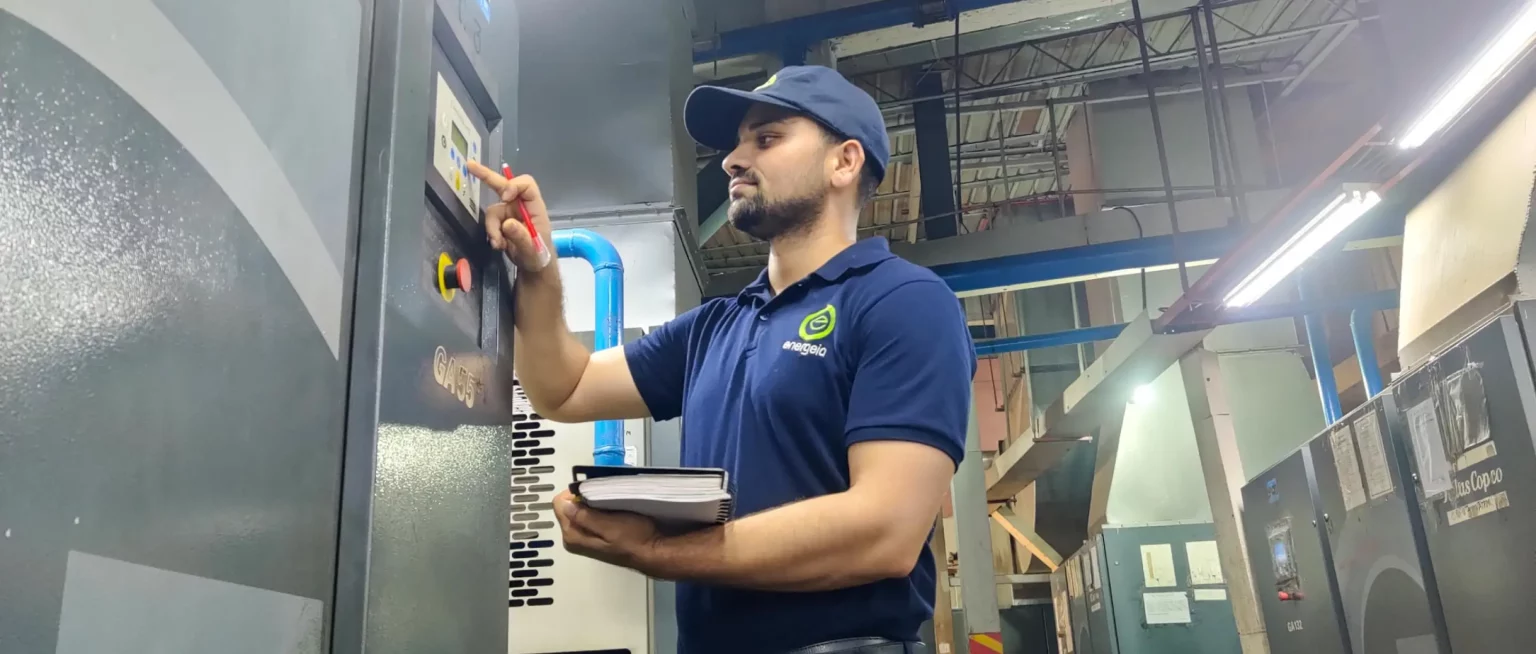 Technician in a blue Energeia uniform inspecting and adjusting a control panel on an industrial machine in a factory.